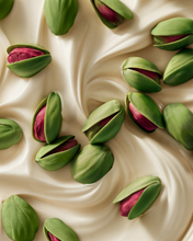 Load image into Gallery viewer, Fresh green pistachio shells with pinkish-red inner nuts scattered across a creamy off-white swirl background.
