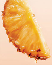 Load image into Gallery viewer, A close-up of a glossy, juicy pineapple slice with a single drop of liquid hanging from the tip, set against a solid pale peach-pink background.
